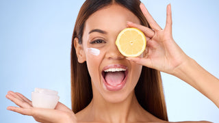 Woman, moisturizer cream and lemon for natural skincare, beauty and vitamin C against blue studio background. Portrait of happy female holding citrus fruit, creme or lotion for healthy organic facial