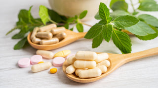 Supplement capsules and pills in spoon on wood surface with mint leaves