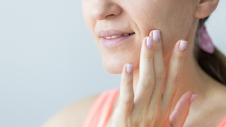 Young smiling woman gently touching her face with fingers. wrinkles, problem dry skin with big pores. Skin care concept.