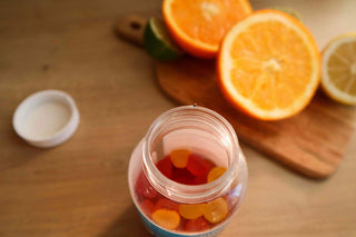 Bottle of Red and Yellow Fruit Gummy Supplements Next to Orange and Lemon on Cutting Board